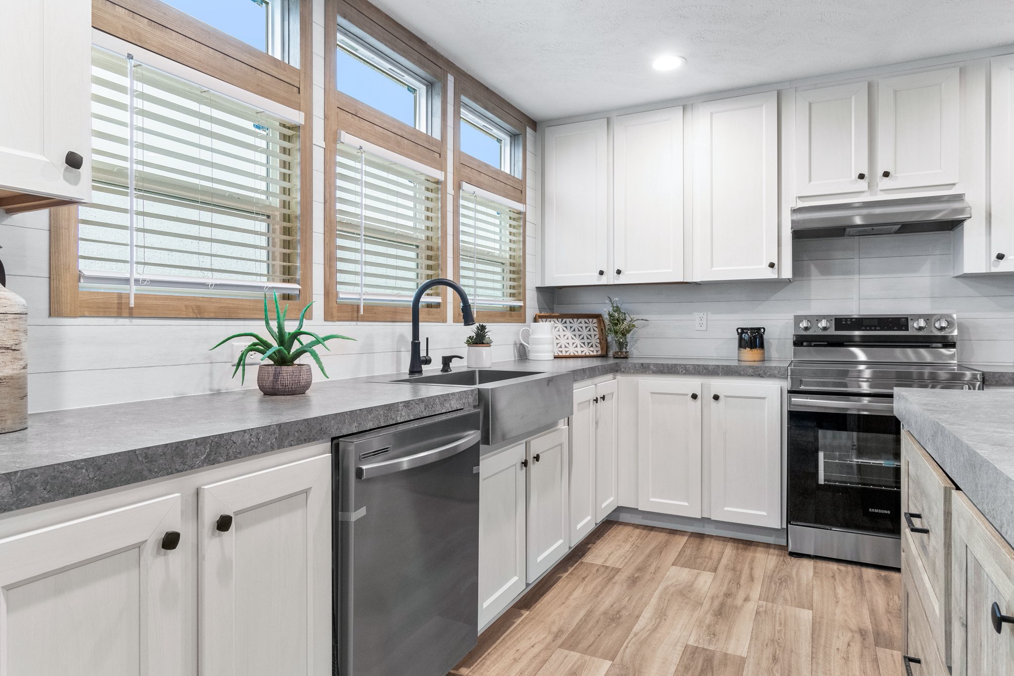 Modern kitchen with white cabinets, stainless steel appliances, and a farmhouse sink. Large windows add natural light. Wood floor provides warmth.