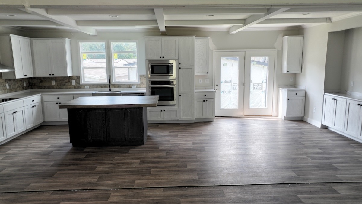 Spacious kitchen with white cabinets, dark central island, stainless steel appliances, and large windows. Light wood flooring adds warmth and openness.