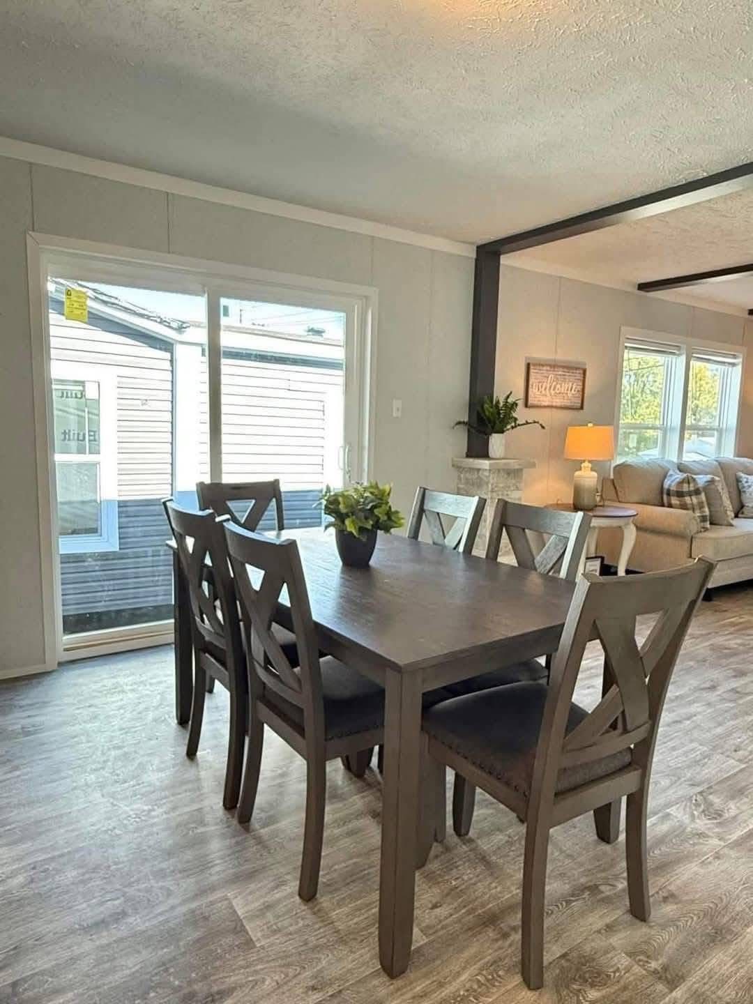 Cozy dining area with a dark wood table and six chairs, a plant centerpiece. Bright room with sliding glass doors, soft gray walls, and inviting decor.
