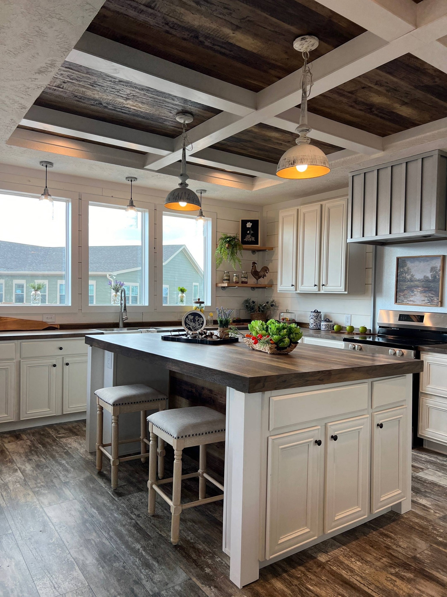 Warm, rustic kitchen with off-white cabinets, dark wooden counters, and a central island with stools. Cozy lighting and decor create a welcoming atmosphere.