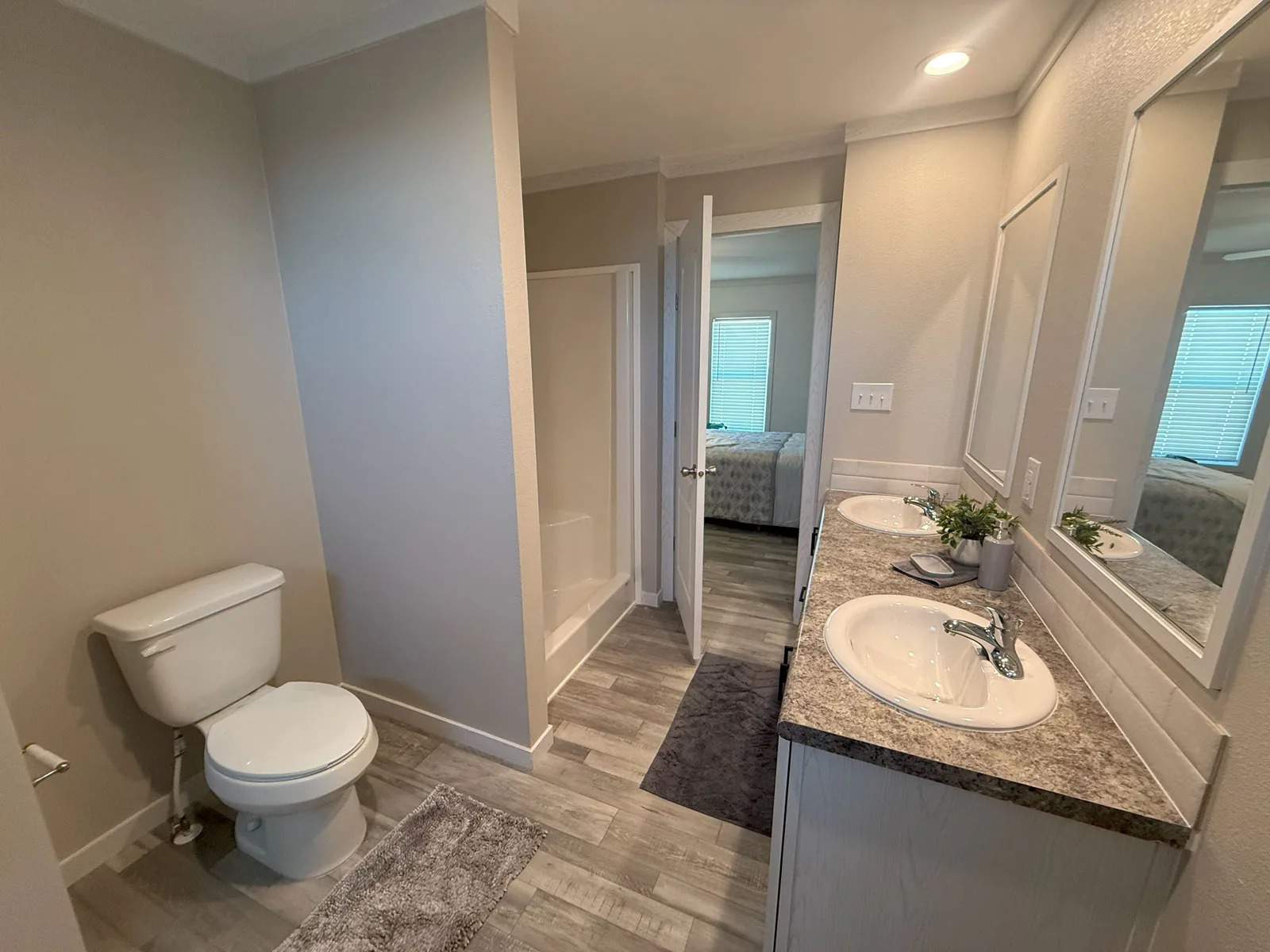 Bathroom with a modern design, featuring dual sinks on a granite countertop, large mirrors, a toilet, and a shower. Neutral tones create a calm atmosphere.