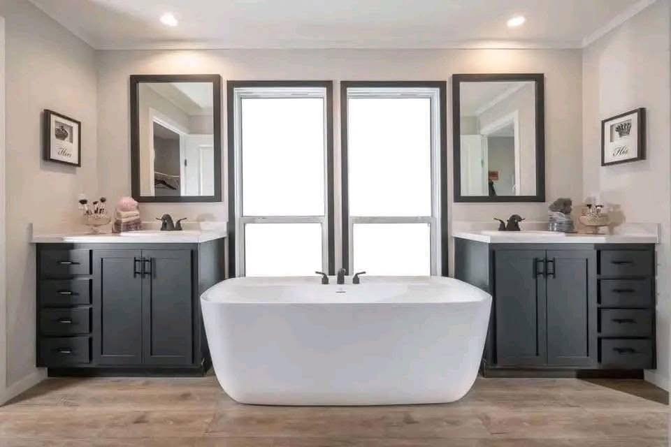 Modern bathroom with a freestanding white bathtub centered between two dark wood vanities. Minimalist decor with bright lighting and two mirrors.