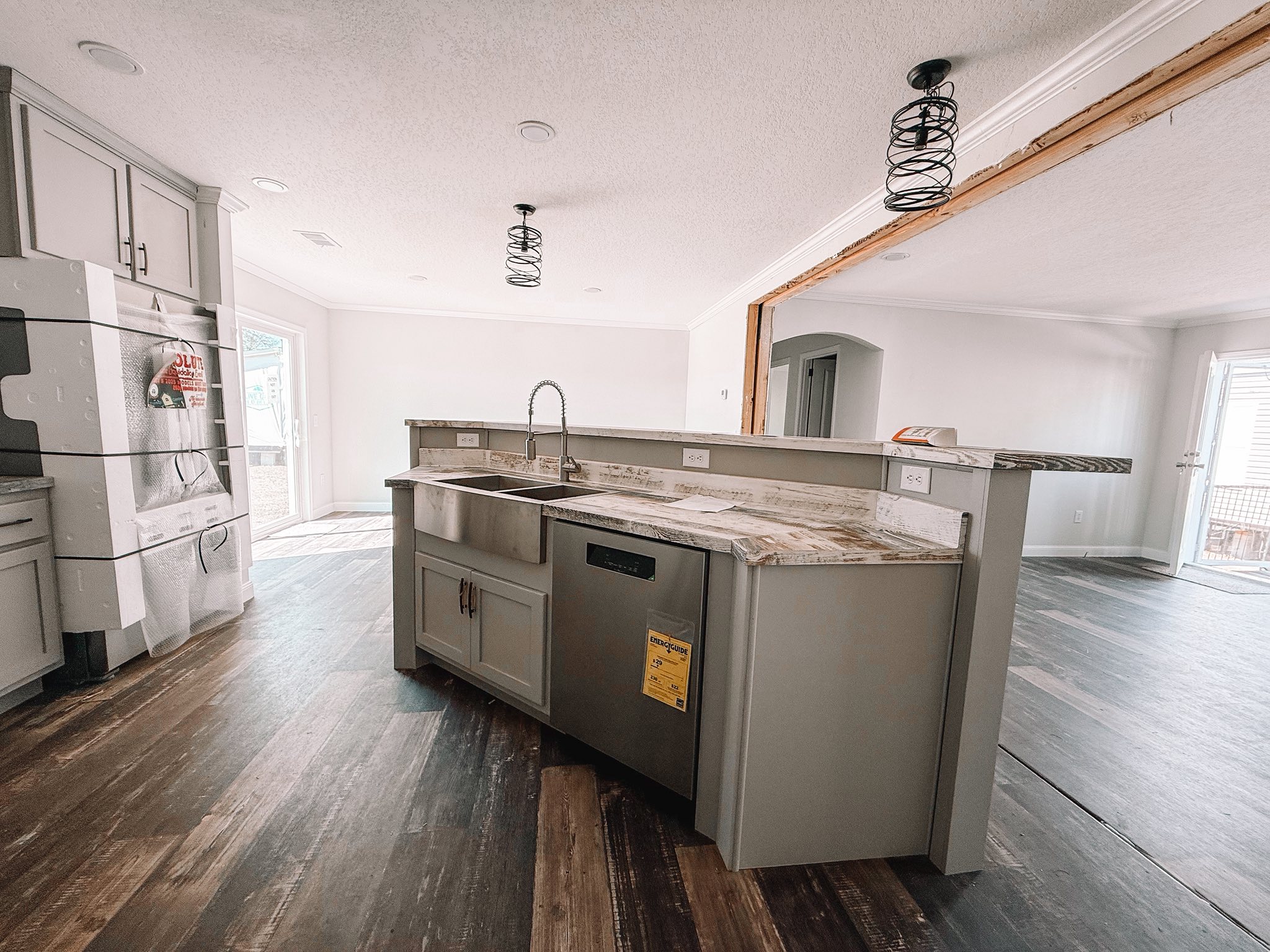 Modern kitchen with an island featuring marble countertops, a stainless steel sink, and new appliances. The open, airy space has wooden floors and pendant lights.