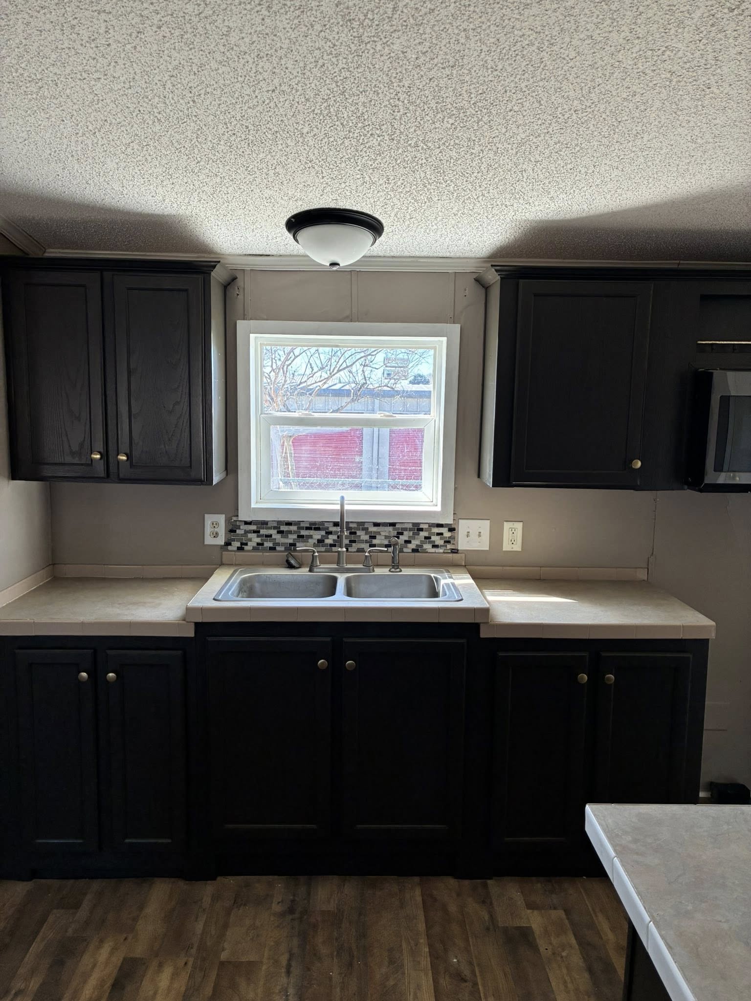 A kitchen interior with dark cabinets, a stainless steel double sink, and a checkered backsplash under a window, creating a clean, modern feel.