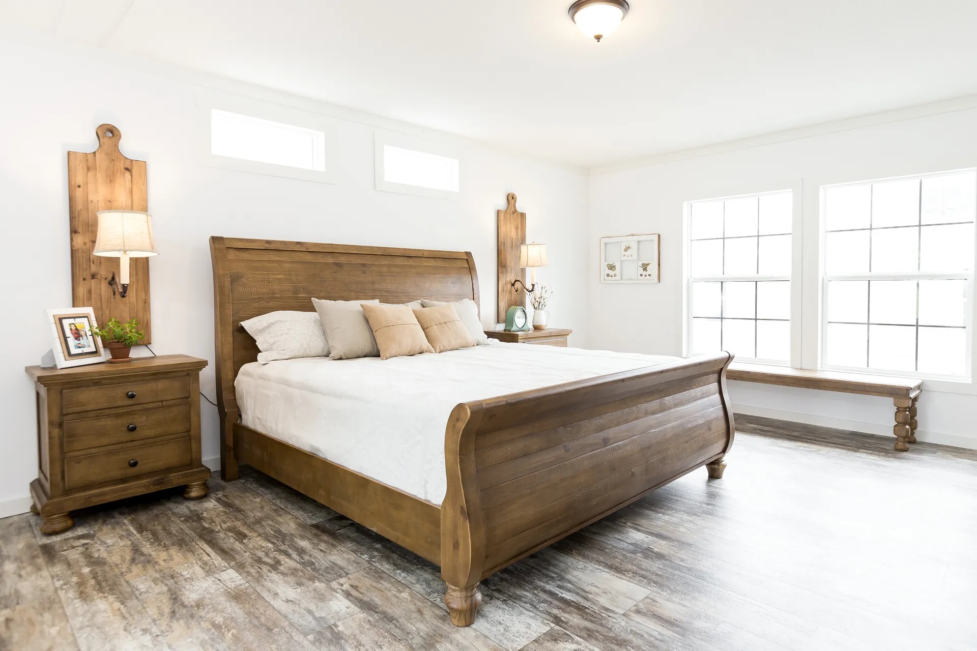 Spacious bedroom with a rustic wooden bed, matching nightstands, and bright natural light from large windows. The room is serene and inviting.