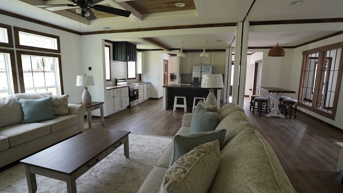 Spacious open-concept living room and kitchen with beige sofas, wooden floors, and a central island. Large windows provide natural light, creating a cozy, inviting atmosphere.