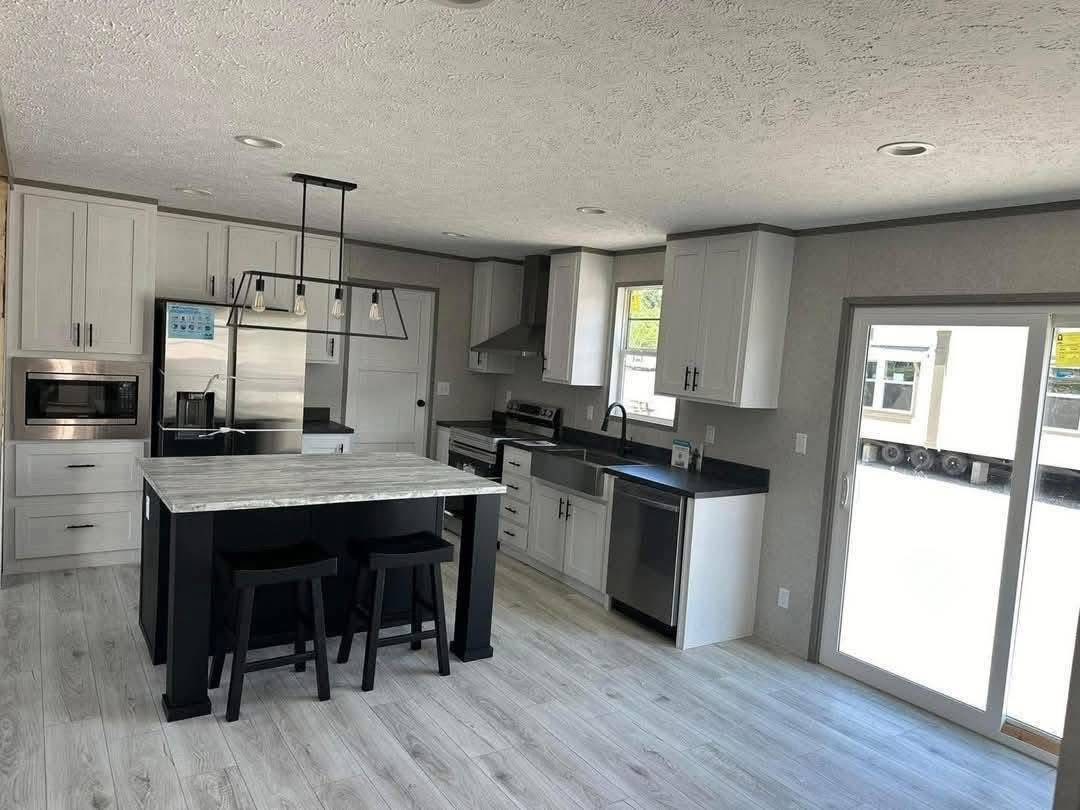 Modern kitchen with white cabinets, black countertops, stainless steel appliances, and an island with two stools. Bright, minimalistic, and inviting.