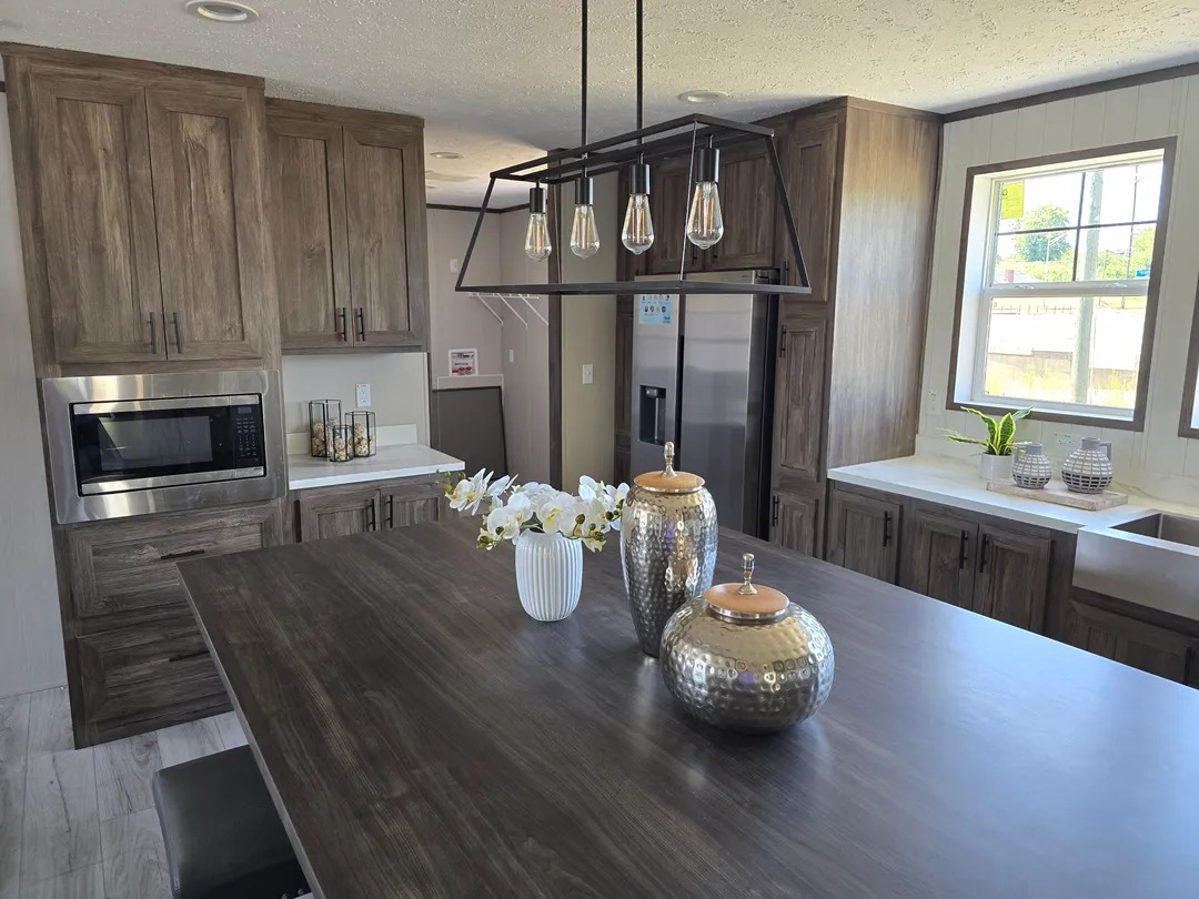 Modern kitchen with wood cabinets, stainless steel appliances, large island with decorative vases, pendant lighting, and a bright, airy vibe.