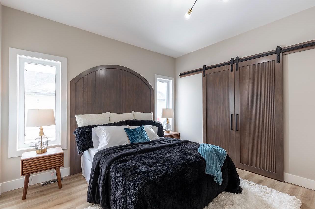 Cozy bedroom with a large wooden headboard, black and white bedding, and accent pillows. Two lamps on wooden nightstands. Sliding barn doors add a rustic touch.