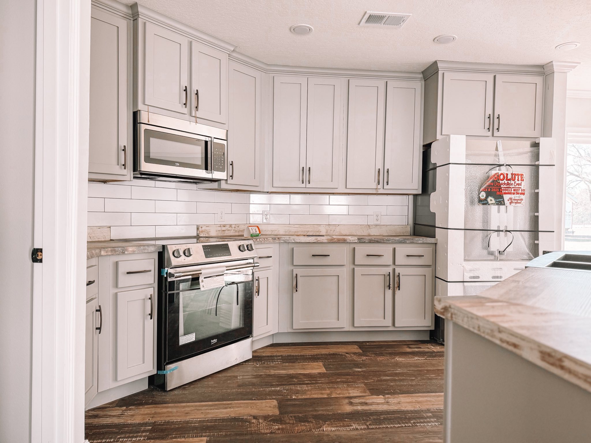 Modern kitchen with gray cabinets, tile backsplash, and wooden floor. Stainless steel appliances include an oven and microwave, creating a sleek and tidy atmosphere.