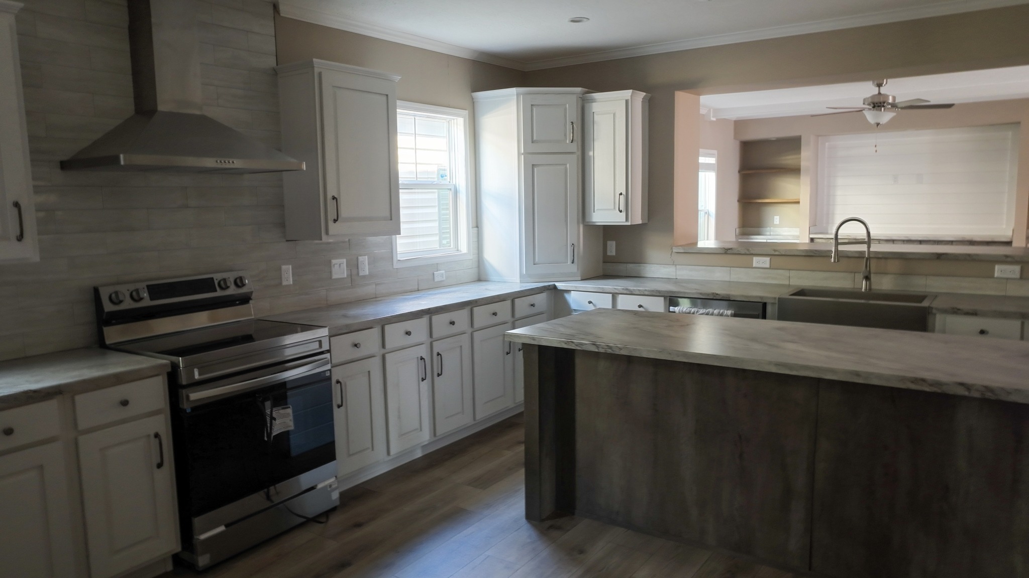 Spacious kitchen with brown and white cabinetry, stainless steel range hood and stove, large island, and farmhouse sink. Ample natural light.