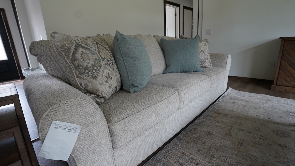 A beige sofa with textured upholstery features patterned and plain teal cushions. It sits on a light rug, creating a calm, inviting atmosphere in the room.