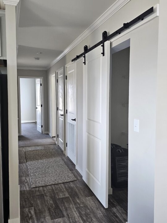 A bright hallway with a sliding barn door partially open, revealing a closet. It has wooden floors, light walls, and multiple doors, creating a modern, minimalistic feel.