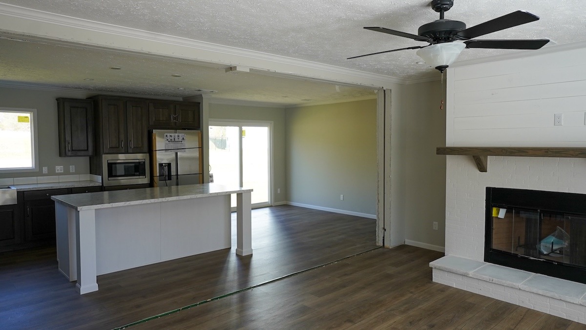 Open-concept living space featuring a modern kitchen with dark cabinets and an island, a bright dining area, a ceiling fan, and a cozy fireplace.