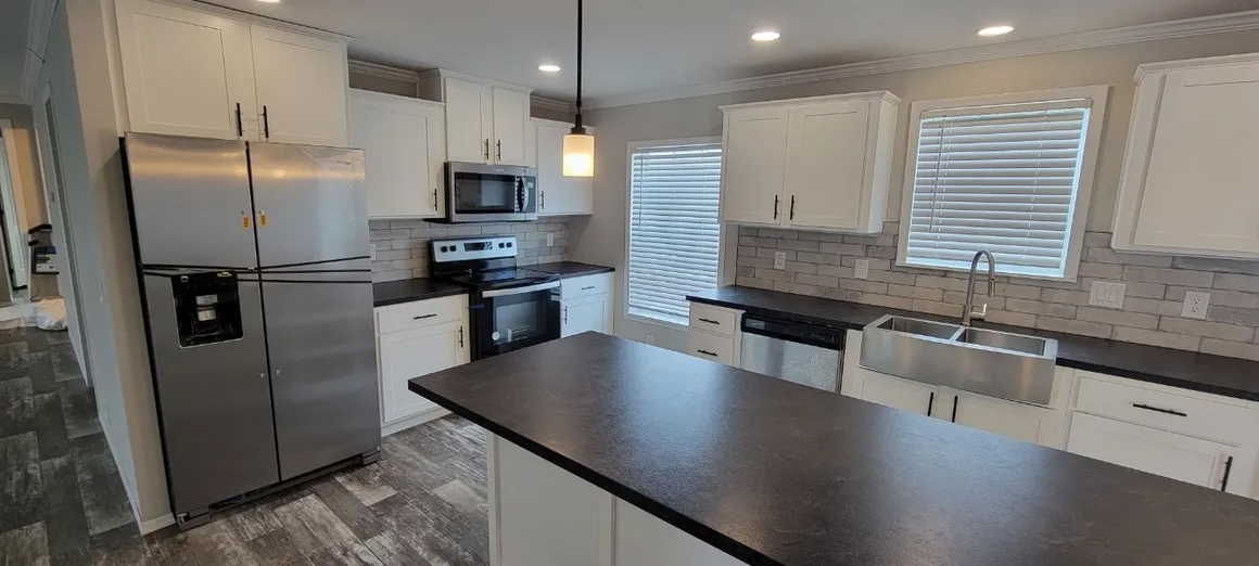 Modern kitchen with white cabinets, stainless steel appliances, and gray countertops. Central island and pendant light create a sleek, minimalist feel.