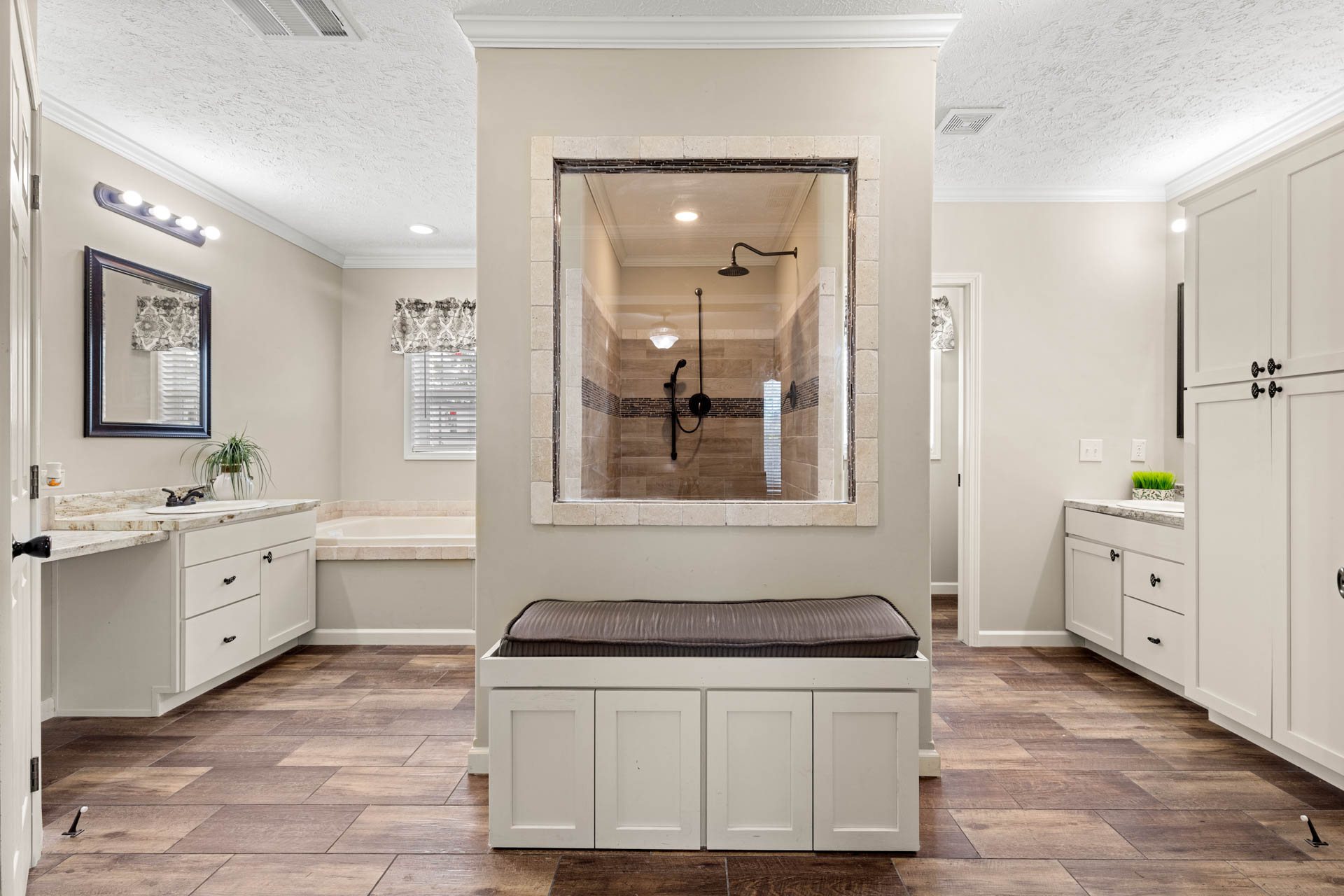 Spacious bathroom with wood floors, featuring a central open shower with glass panel, flanked by two white vanities, evoking a modern, clean vibe.