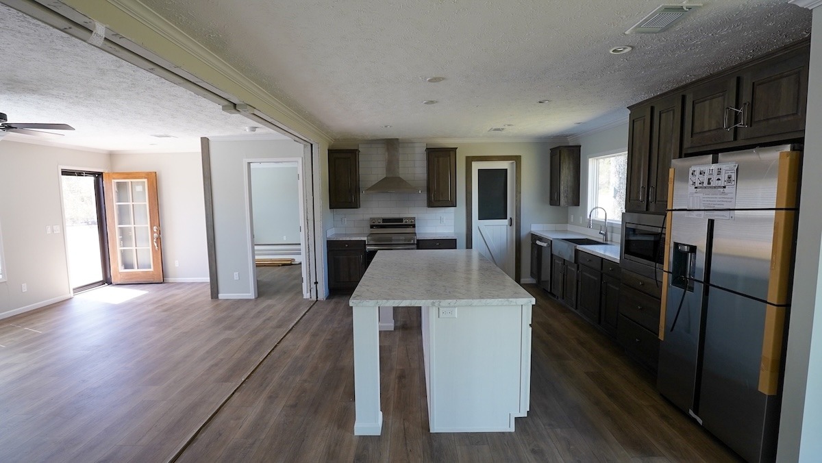 Spacious modern kitchen with dark wood cabinets, large center island, stainless steel appliances, and light wood flooring. Bright with natural light.