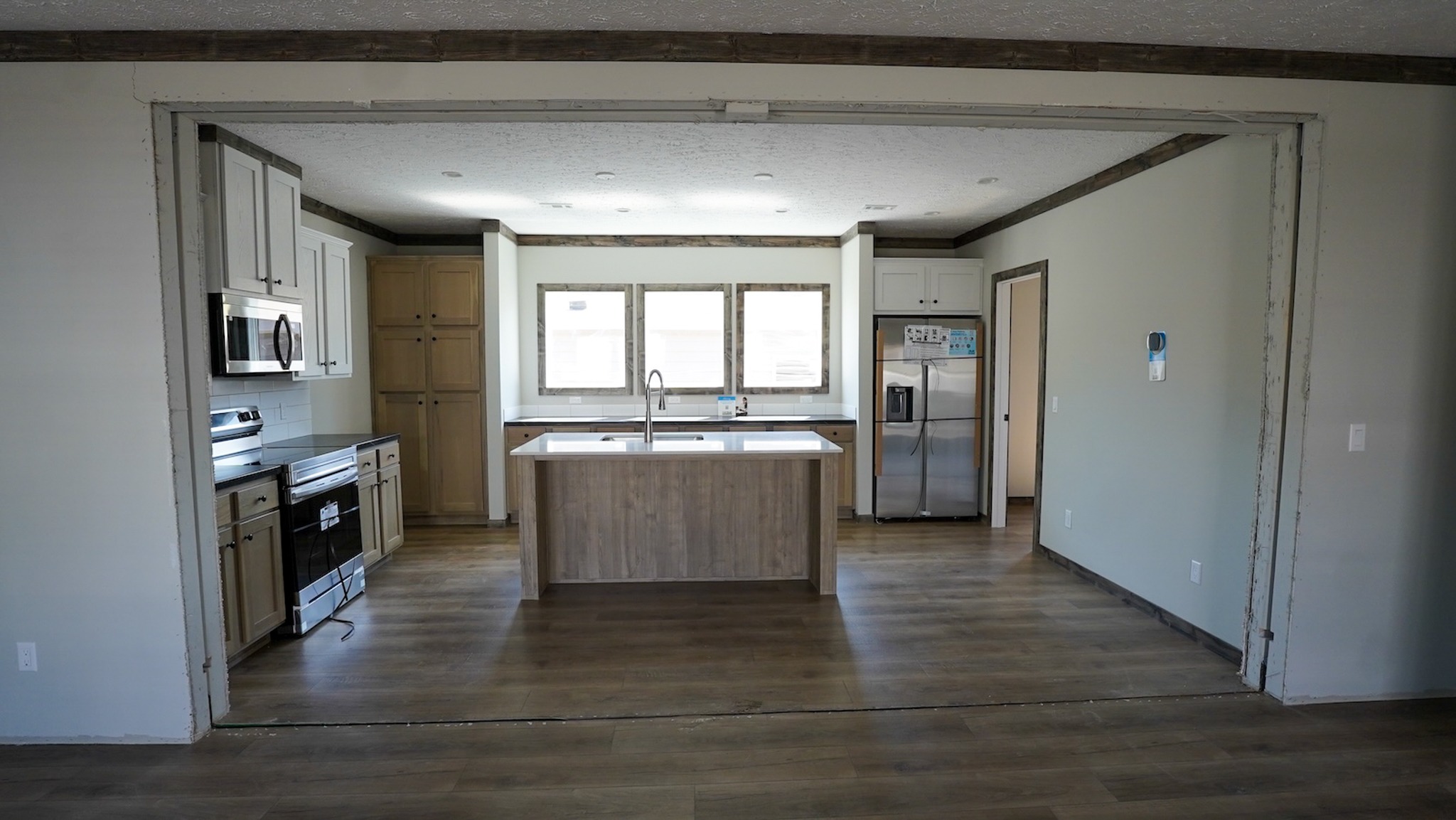 Modern kitchen with wood flooring, central island with sink, stainless steel appliances, white cabinets, and large windows. Bright and spacious atmosphere.