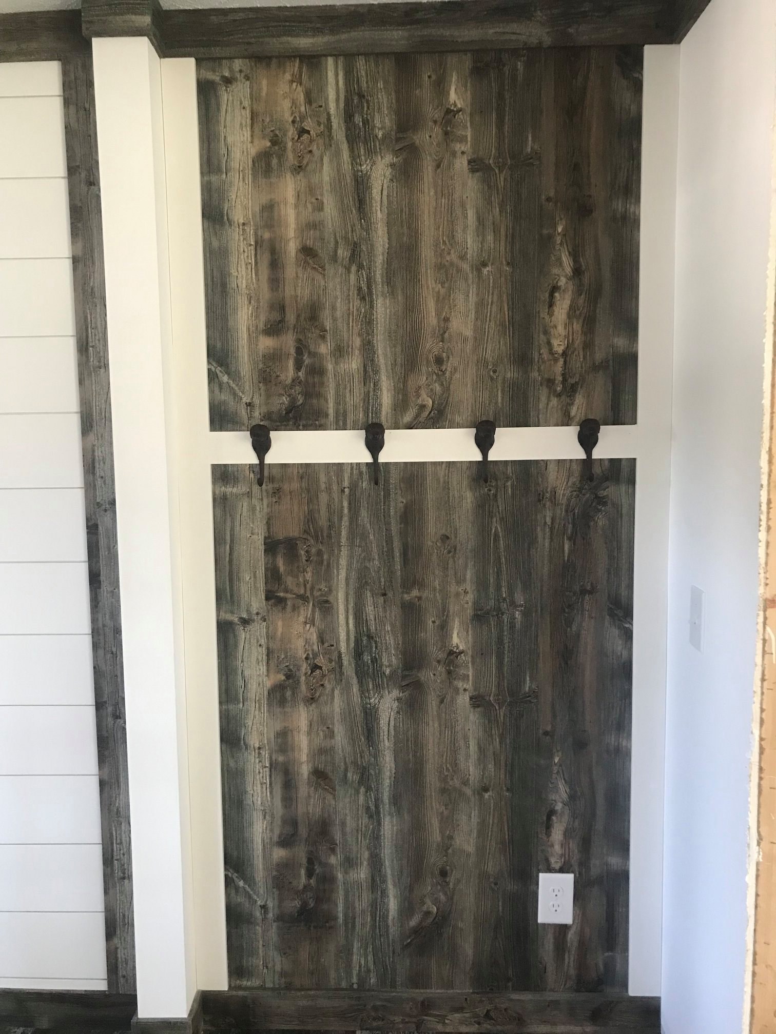 Rustic wooden wall panel with rich, weathered texture, featuring four black metal hooks. Warm, earthy tones create a cozy, natural atmosphere.