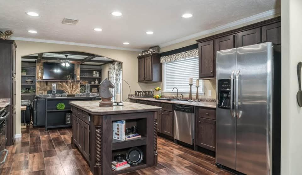 Spacious kitchen with dark wood cabinets, stainless steel fridge, and dishwasher. Central island features open shelving. Warm, ambient lighting.