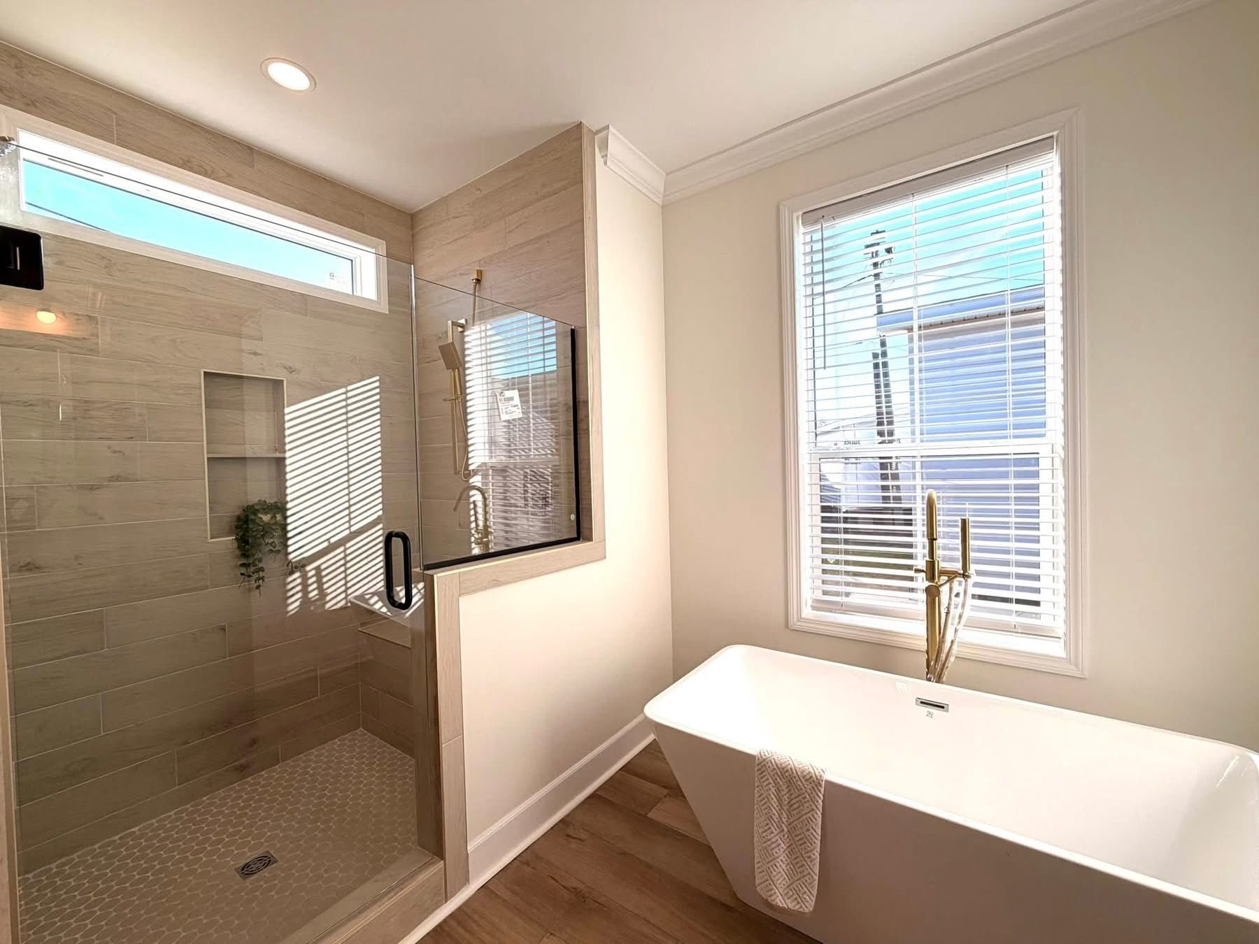 Bright bathroom with a glass-enclosed shower on the left and a freestanding bathtub on the right. Sunlight streams through a window, creating a serene ambiance.
