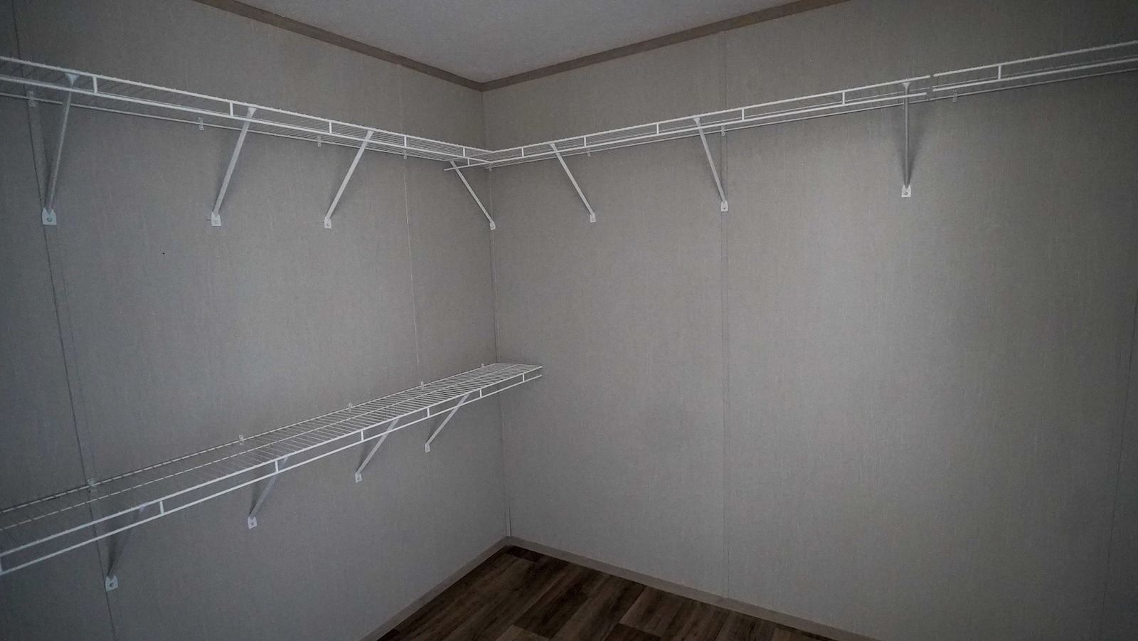 Empty walk-in closet with white wire shelves along beige walls, creating a clean, minimalist look. Wooden floor adds warmth and texture.