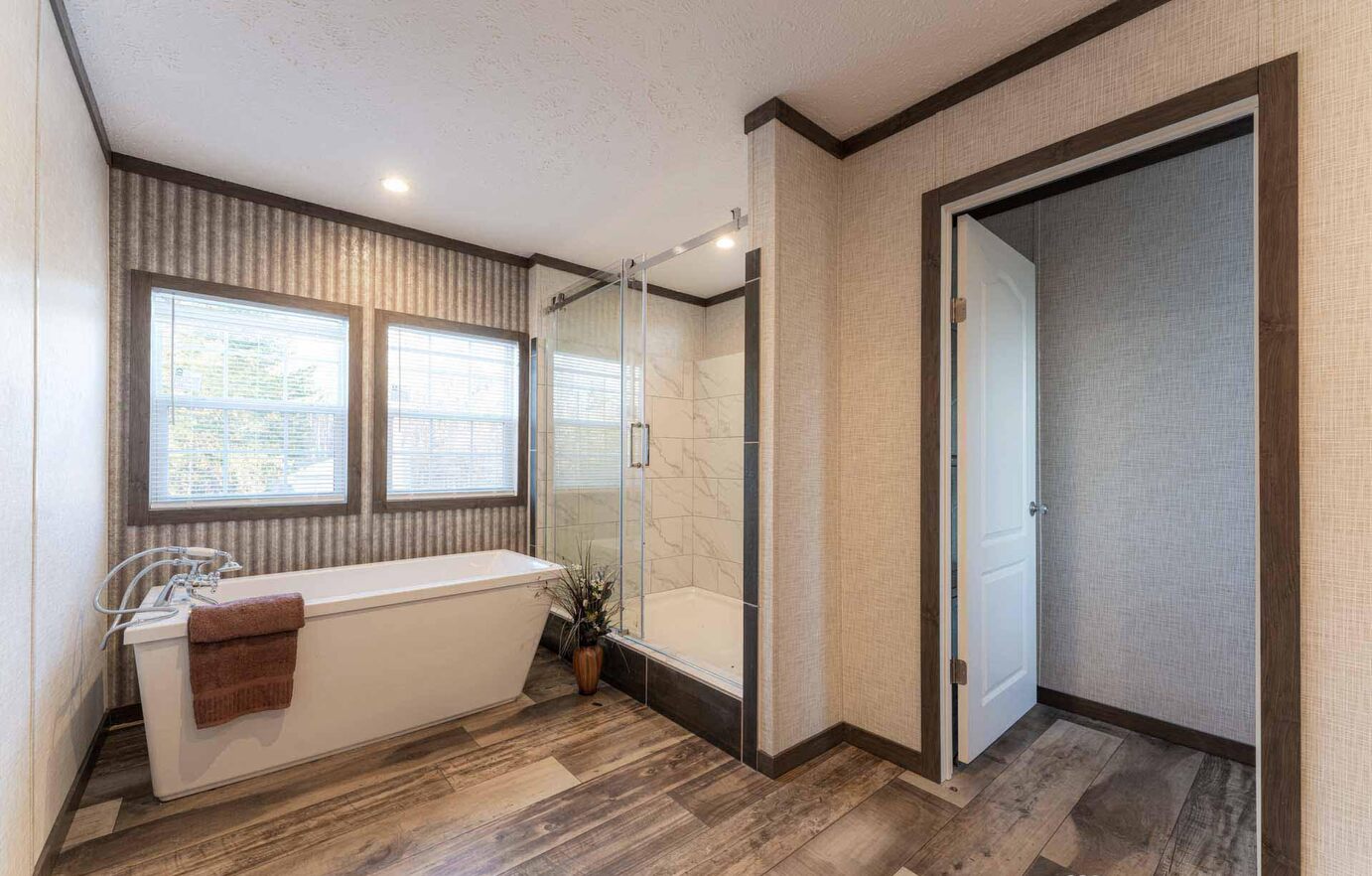 Modern bathroom featuring a freestanding bathtub with a brown towel, a glass-enclosed shower, and two large windows; warm, inviting ambiance.