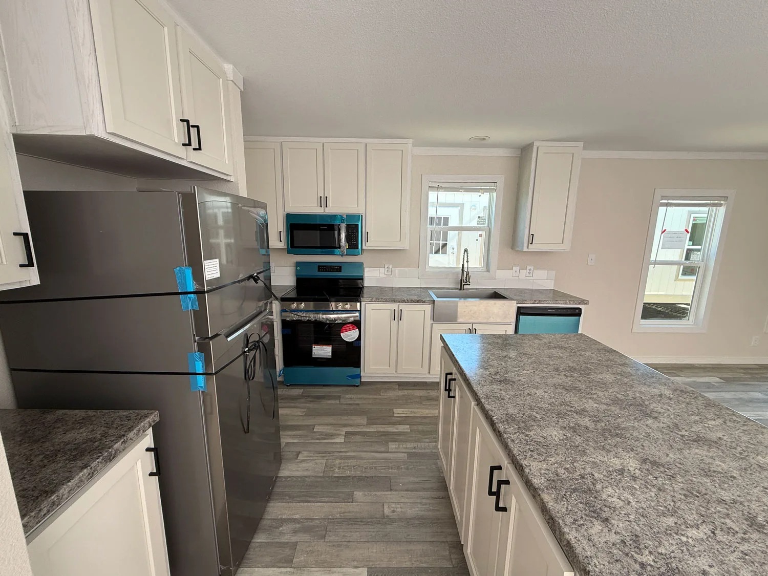 Modern kitchen with light cabinets, stainless steel appliances, and a spacious gray island. Sunlit windows create a bright, welcoming atmosphere.
