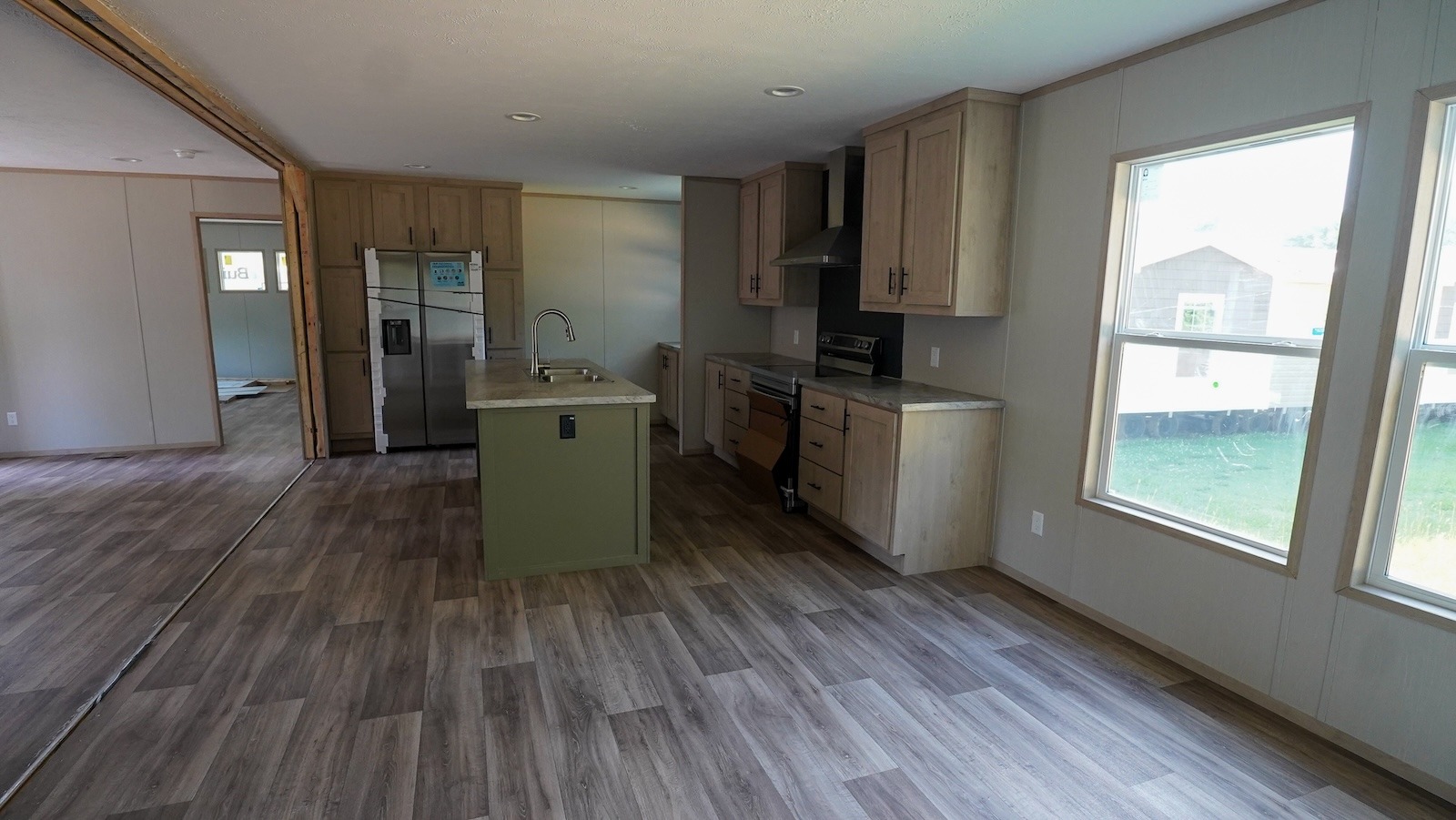 Spacious, modern kitchen and dining area with wood flooring, light wood cabinets, stainless steel appliances, and large windows providing ample natural light.