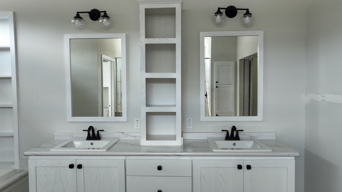 Elegant bathroom vanity with dual sinks, black faucets, and white cabinets. Two mirrors and symmetrical lighting add a modern, minimalist touch.