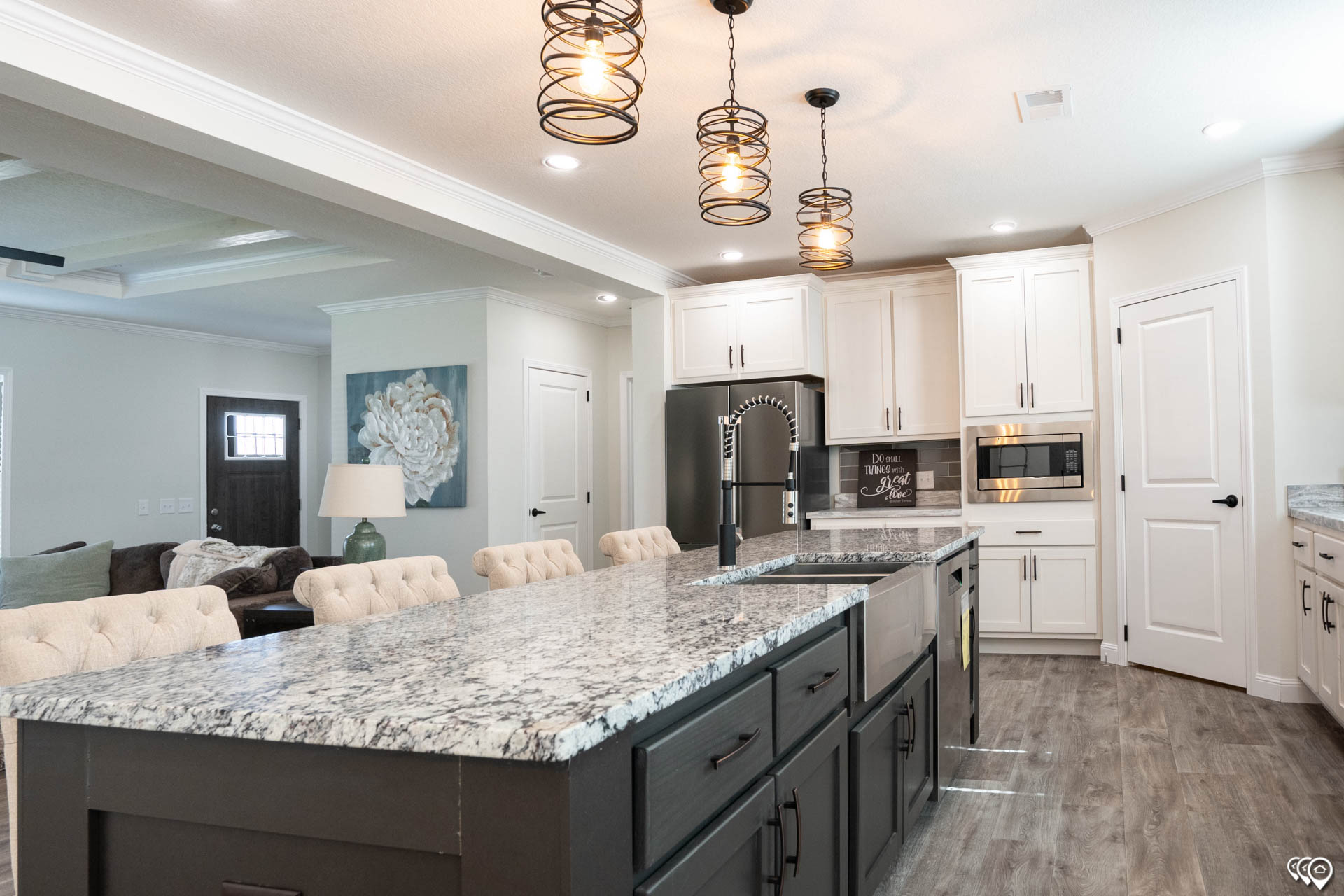 Spacious kitchen with a long marble island, dark cabinets, and modern pendant lights. White cabinetry, stainless steel appliances, and cozy seating.