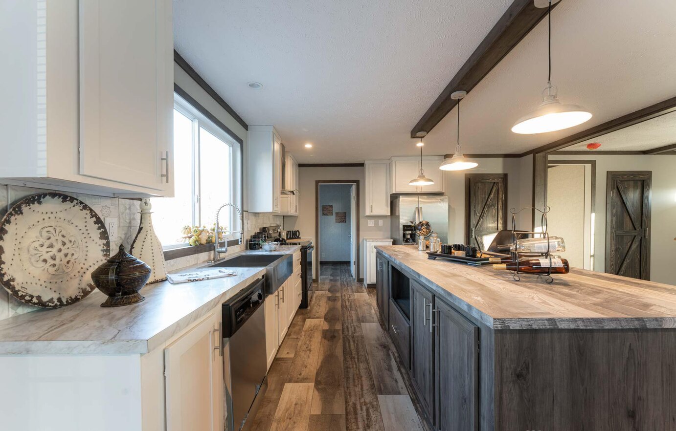 Spacious modern kitchen with a large island, wood flooring, and pendant lighting. White cabinets and stainless steel appliances add elegance.