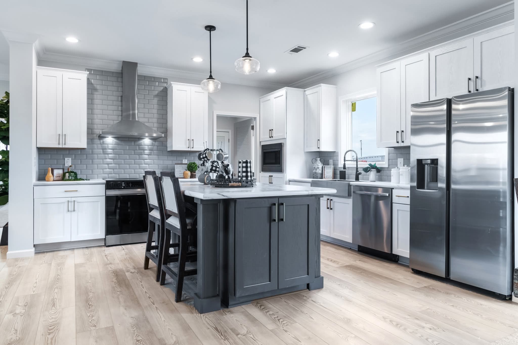 Modern kitchen in neutral tones featuring white cabinets, stainless steel appliances, gray backsplash, and a dark island with bar stools. Bright and sleek ambiance.