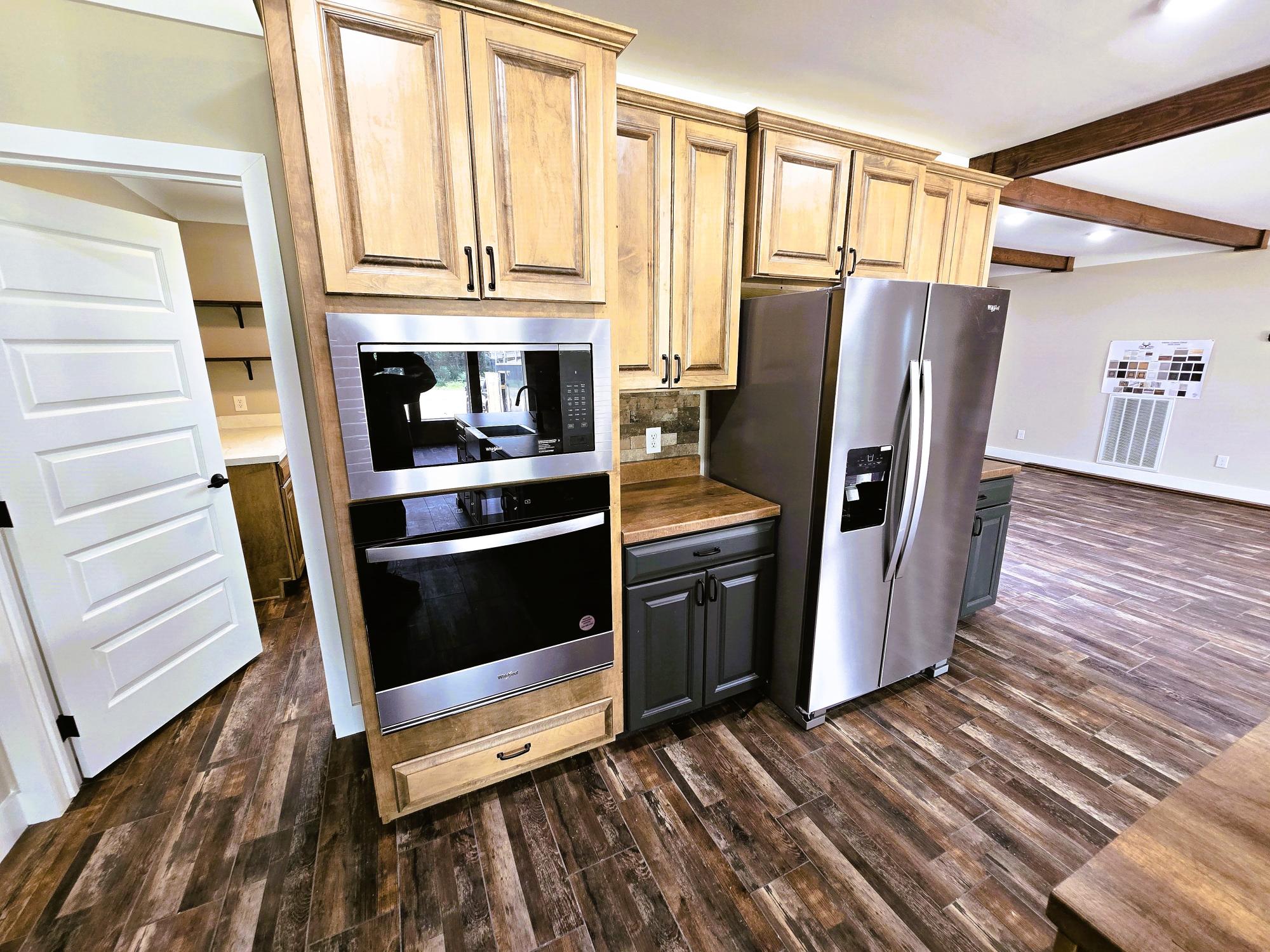 Modern kitchen with stainless steel appliances, including a double oven and refrigerator. Wooden cabinets and dark countertops on hardwood floors. Cozy and inviting.