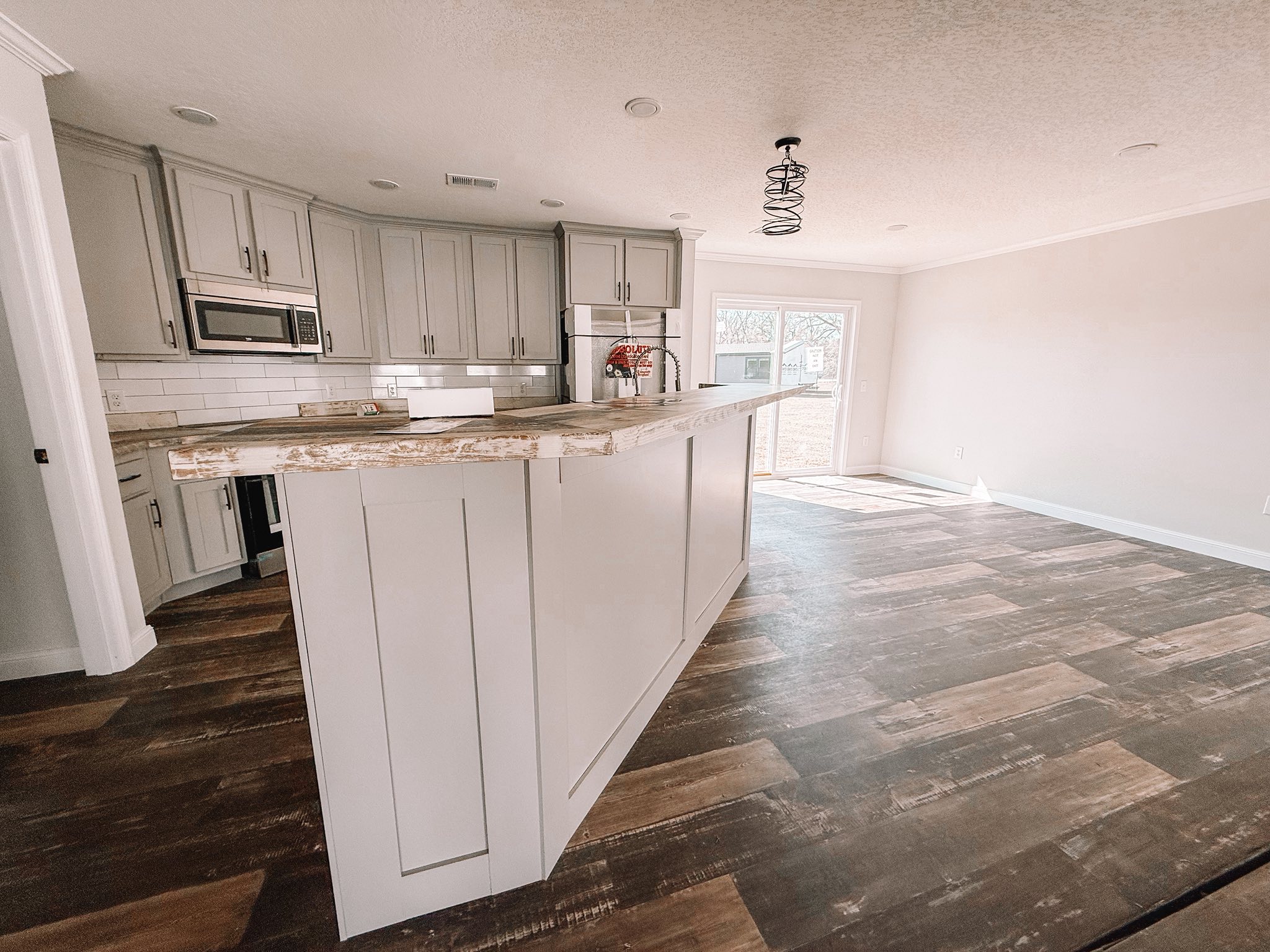 Spacious kitchen with light gray cabinets, a rustic wood island, and dark hardwood floors. Sunlight streams through a glass door, enhancing a cozy, inviting atmosphere.