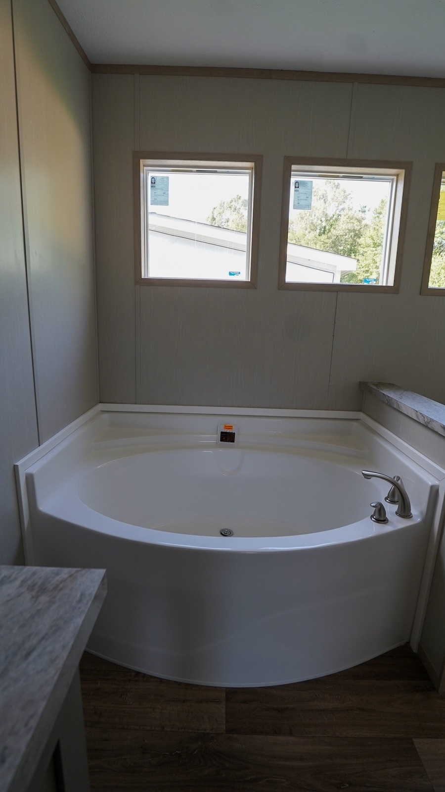 Corner bathtub in a modern bathroom with three small windows above. Sunlight filters in, creating a tranquil ambiance. Wood floors add warmth.