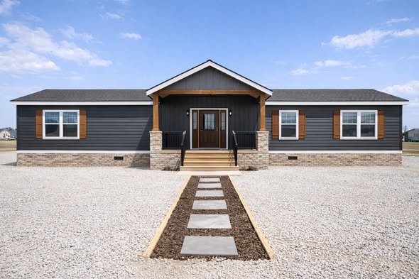 A modern, single-story dark gray home with white trim and brown shutters, features a centered wooden entrance. A stone path leads to the porch, set in a gravel yard on a clear day.