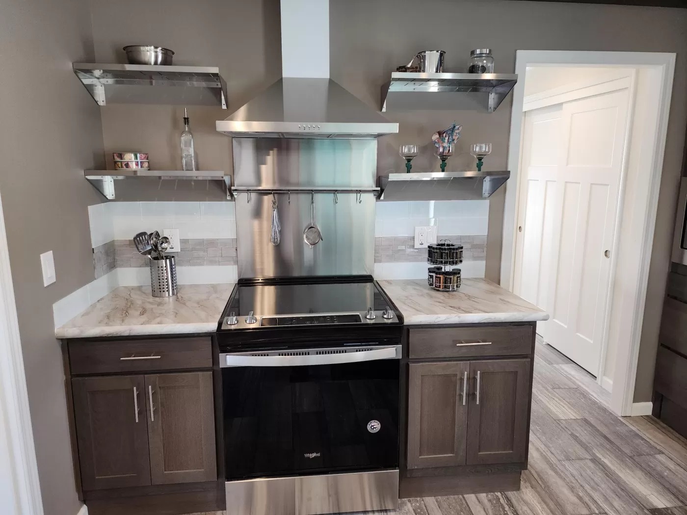 Modern kitchen with a stainless steel oven and range hood, flanked by wooden cabinets. Open shelves hold cookware and décor, creating a clean, organized look.