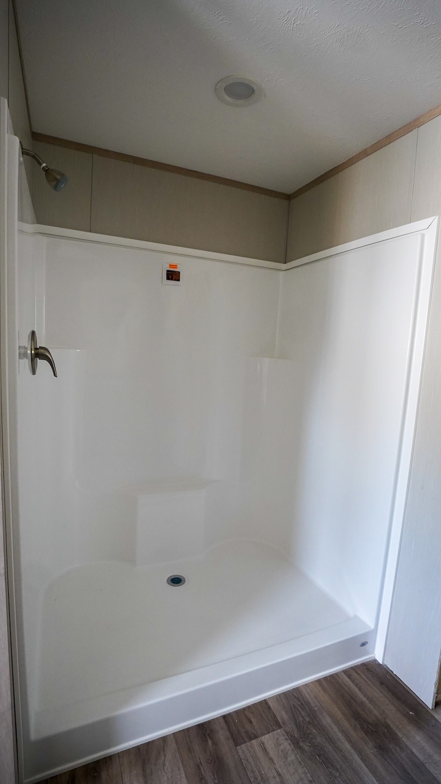A spacious, modern white shower with smooth walls, a built-in corner seat, and a chrome faucet. The flooring is wood-like, adding warmth to the minimalist design.