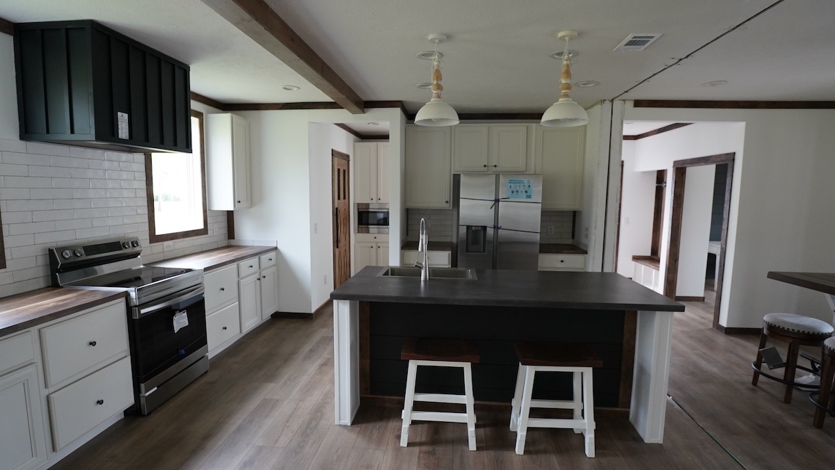 Modern kitchen with a large island, two pendant lights, and wooden stools. Stainless steel appliances and white cabinets create a clean, airy feel.