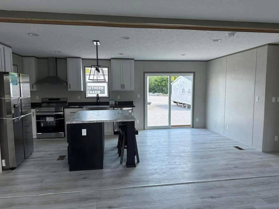 Modern kitchen and dining area with light gray flooring. Features stainless steel appliances, a central island with bar stools, and sliding glass doors leading outside. Bright and spacious.