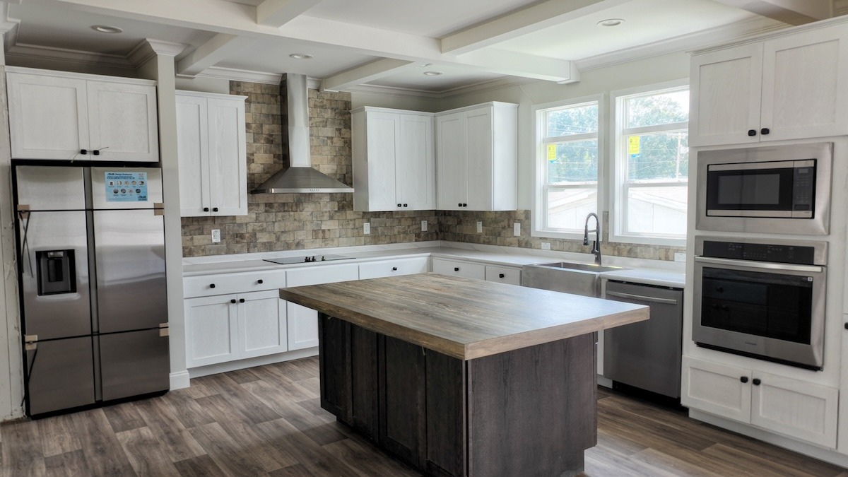 Spacious kitchen with white cabinets, a wooden island, stainless steel appliances, and tiled backsplash. Bright and modern with natural light.