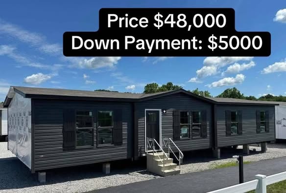 A dark gray manufactured home with multiple windows is set against a blue sky with clouds. Text above lists price as $48,000 with $5,000 down payment.