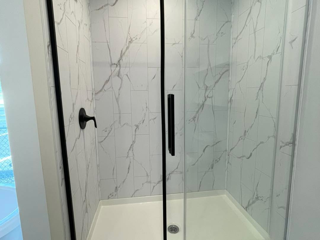 Modern shower with glass doors, black hardware, and white marble-patterned tiles. Bright and sleek design conveys a fresh, clean feel.