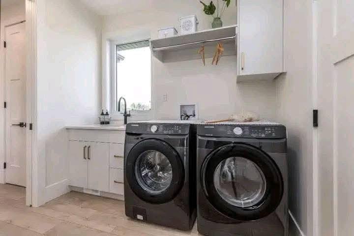 A modern laundry room with a sleek black washer and dryer set side by side. Above, a shelf and cabinet hold decor, conveying a clean, organized space.