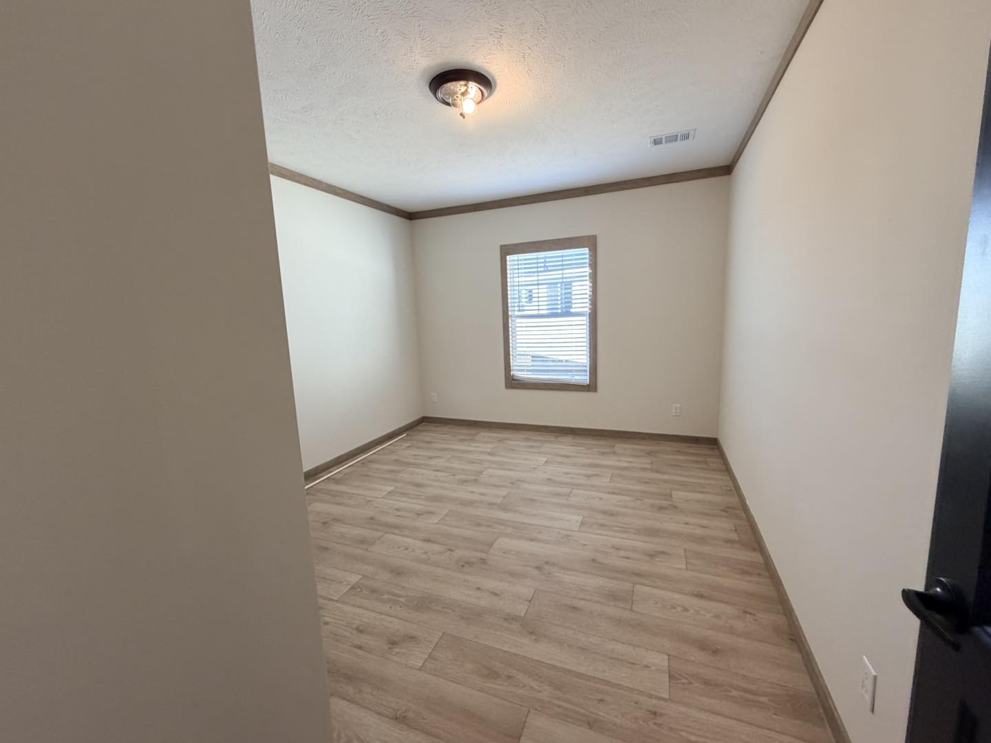 Empty room with light wood flooring, cream walls, and a single window with blinds. Ceiling light fixture emits soft warm glow, creating a serene atmosphere.