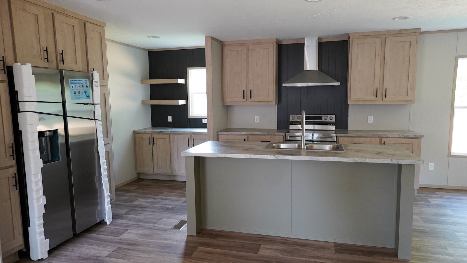 Spacious kitchen with wooden cabinets, marble countertops, and a stainless steel fridge. An island with a sink and stove create a modern feel.