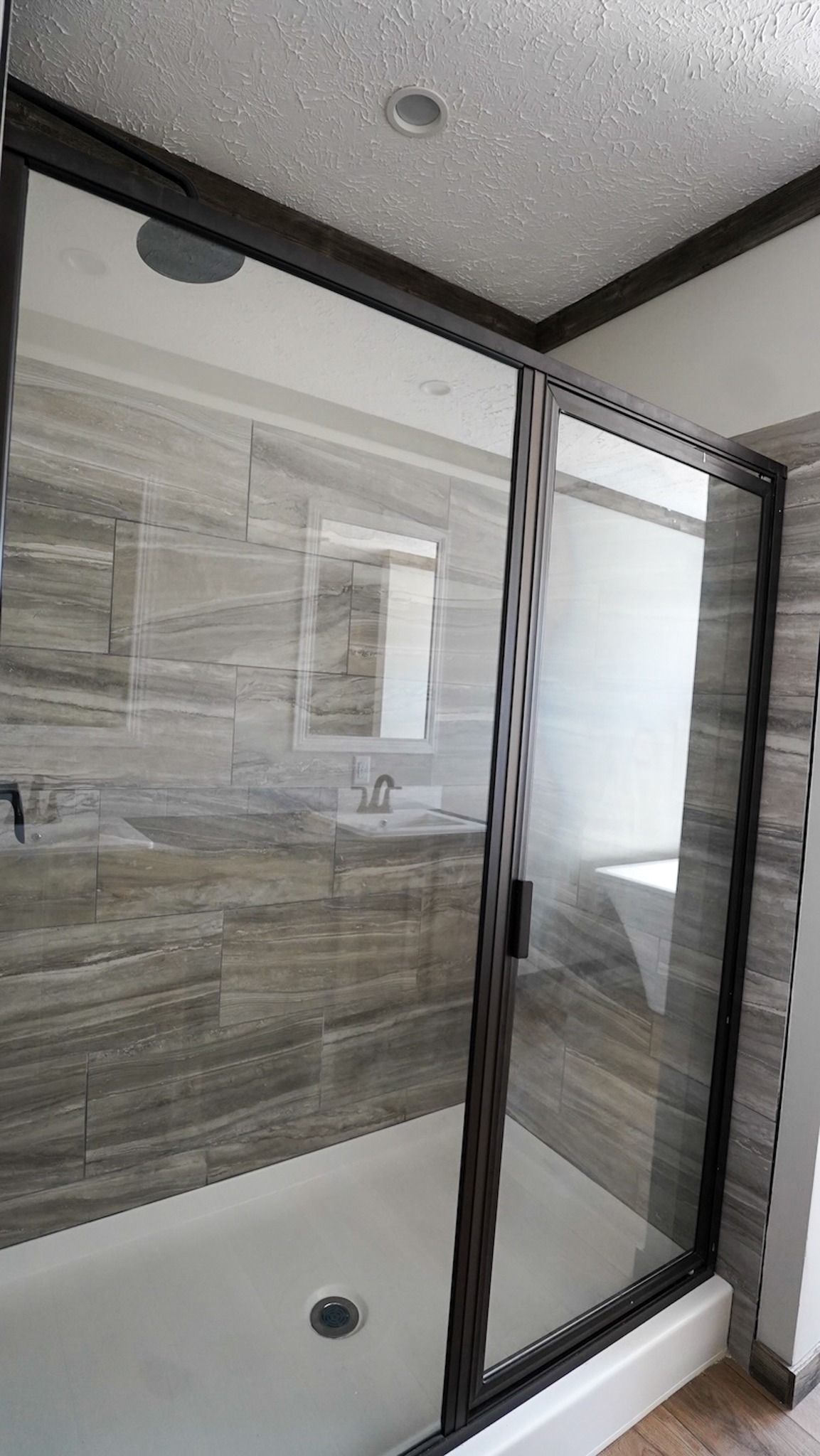 Modern shower with glass doors, featuring gray stone-tiled walls. The sleek design and neutral tones create a clean, contemporary feel.