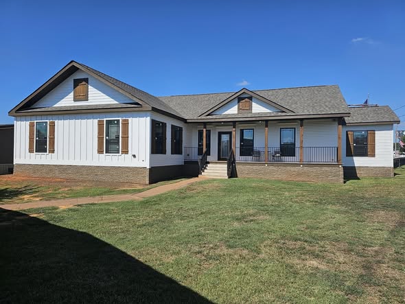 Single-story house with white siding, brown shutters, and a gray roof, surrounded by a well-kept green lawn under a clear blue sky.
