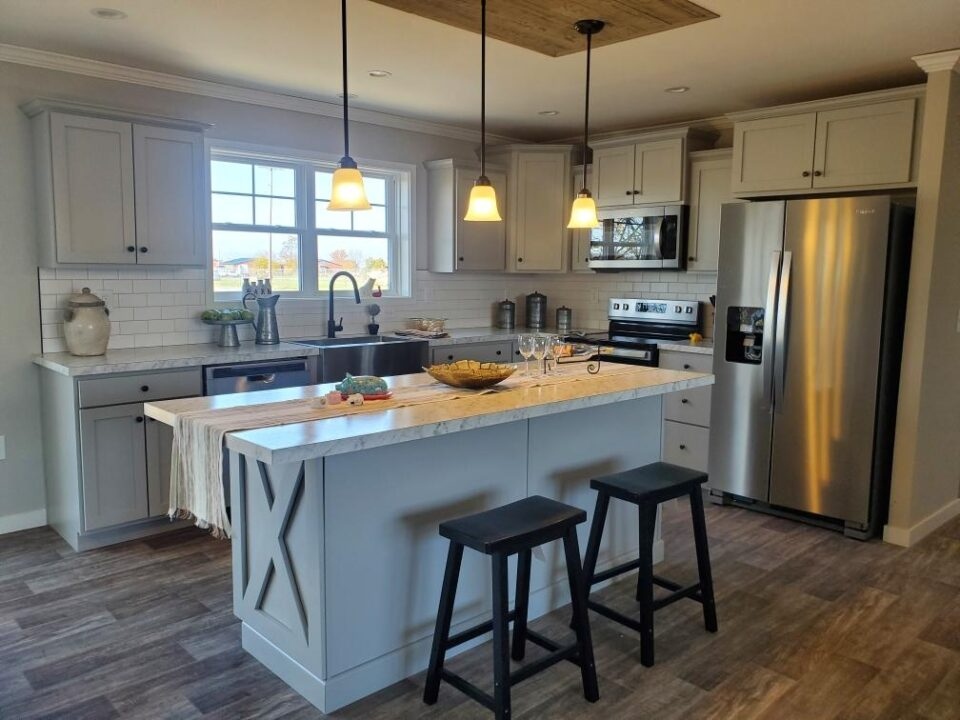 Modern kitchen with gray cabinets, marble island with two black stools, stainless steel appliances, and pendant lights, creating a cozy ambiance.